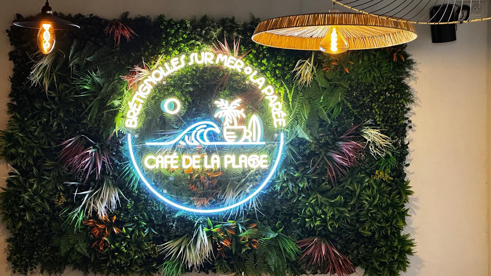 Néon LED Café de la Plage sur un mur végétal